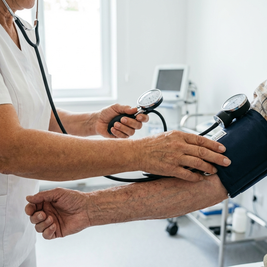 Nahaufnahme von Händen einer erfahrenen Pflegekraft, die behutsam den Blutdruck eines älteren Herrn misst. Heller, sauberer Raum, medizinische Professionalität.