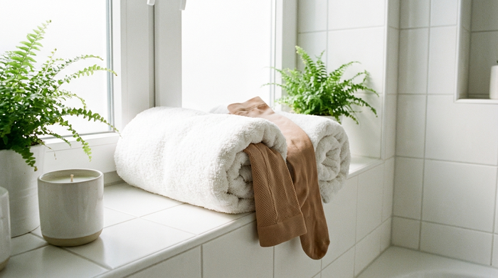 Medizinische Kompressionsstrümpfe, die sanft in ein flauschiges, weißes Handtuch eingerollt sind, um schonend an der Luft zu trocknen. Helles, sauberes Badezimmer mit weißen Fliesen, beruhigende Atmosphäre.