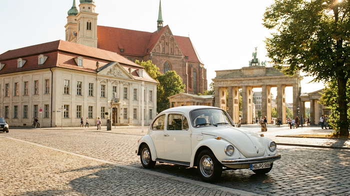 Ein kleines weißes Auto parkt vor einer malerischen Kulisse mit historischen Gebäuden und Kopfsteinpflaster in Potsdam bei strahlendem Sonnenschein.