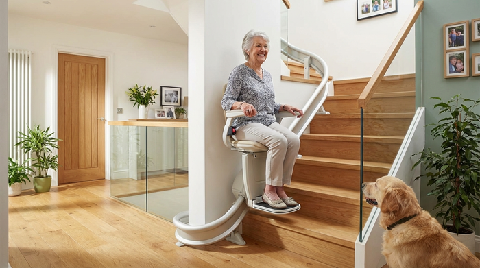Ein moderner Treppenlift in einem gepflegten Einfamilienhaus, eine ältere Dame fährt sicher und lächelnd die Treppe hinauf.