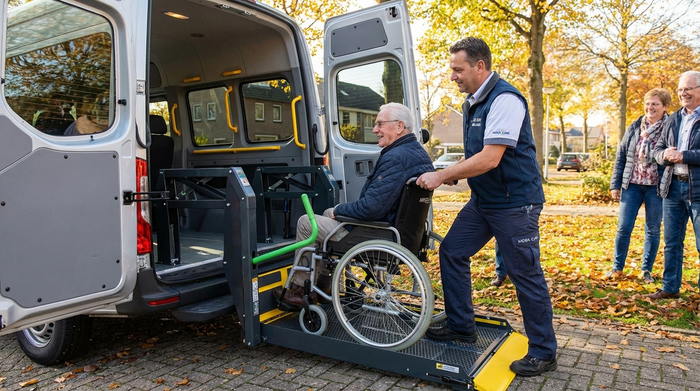 Ein älterer Herr im Rollstuhl wird von einem professionellen Betreuer behutsam über eine sichere Hebebühne in einen geräumigen Transporter geschoben.