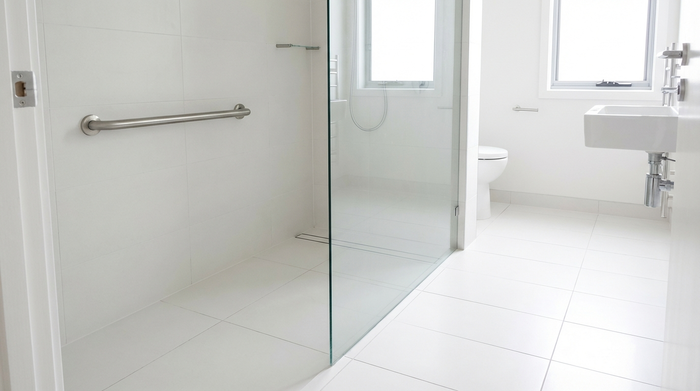 Eine moderne, barrierefreie bodengleiche Dusche in einem hell gefliesten Badezimmer. Ein stabiler Haltegriff ist dezent an der Wand angebracht. Sauber, aufgeräumt, realistisches Interieur ohne Text.