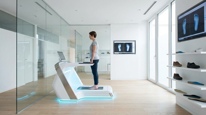 Eine moderne, saubere Praxisumgebung. Ein helles, futuristisch anwirkendes 3D-Scan-Gerät zur Fußvermessung leuchtet dezent blau auf dem Boden eines orthopädischen Fachgeschäfts.