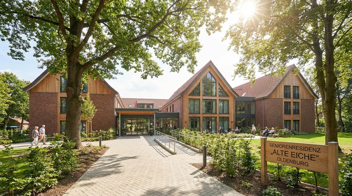 Eine moderne, gepflegte Außenansicht einer Seniorenresidenz im Grünen, typisch für das Oldenburger Umland. Einladender Eingangsbereich mit barrierefreien Wegen und alten Bäumen im Hintergrund.