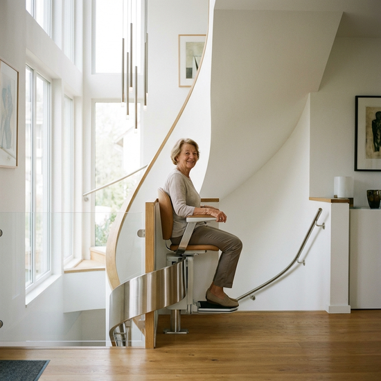 Ein eleganter, moderner Treppenlift in einem gepflegten Einfamilienhaus. Eine ältere Person fährt sicher und entspannt die Treppe hinauf. Helle Beleuchtung, sichere Umgebung.