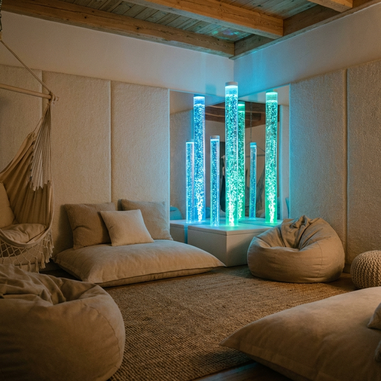 Ein reizarmer Snoezelen-Raum mit gedimmtem Licht, sanft leuchtenden Wassersäulen und bequemen Liegemöglichkeiten. Eine friedliche, beruhigende Stimmung, die zur völligen Entspannung einlädt.