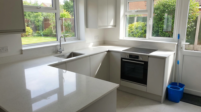 Eine ordentliche, saubere Küche mit glänzenden Arbeitsflächen und frisch geputzten Fenstern, ein Wischeimer und ein Mopp stehen ordentlich in der Ecke.