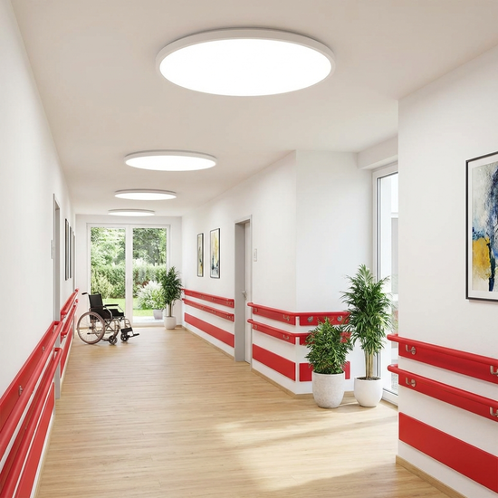 Ein heller, barrierefreier Flur in einer modernen Pflegeeinrichtung. Rote Handläufe bieten einen starken Kontrast zu den weißen Wänden. Tageslichtähnliche Deckenlampen leuchten den Weg schattenfrei aus. Sauber, einladend und fotorealistisch.