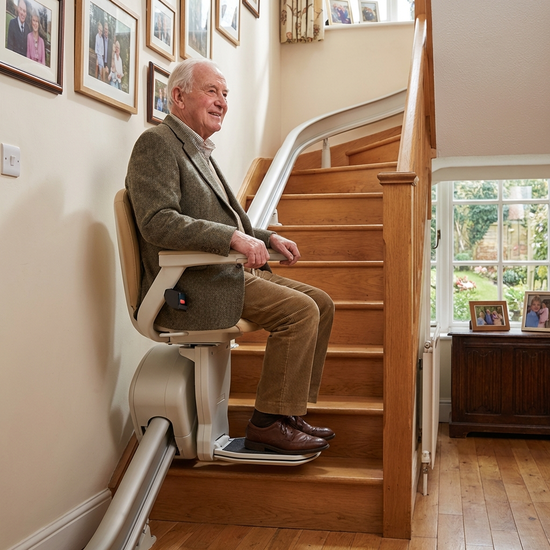Ein älterer Herr fährt sicher und entspannt mit einem modernen Treppenlift die Treppe in seinem Einfamilienhaus hinauf.