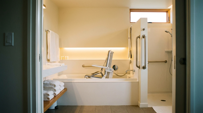 Ein helles, sauberes und barrierefreies Badezimmer mit einem modernen Badewannenlift in einer weißen Badewanne. Frische Handtücher liegen ordentlich bereit. Das Licht ist warm und einladend, realistische Szene ohne Beschriftungen.