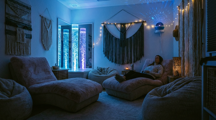 Ein gemütlicher Snoezelen-Raum mit gedimmtem Licht, sanft leuchtenden Wassersäulen in Blautönen und bequemen, weichen Liegesesseln. Eine entspannte, ruhige und therapeutische Stimmung.