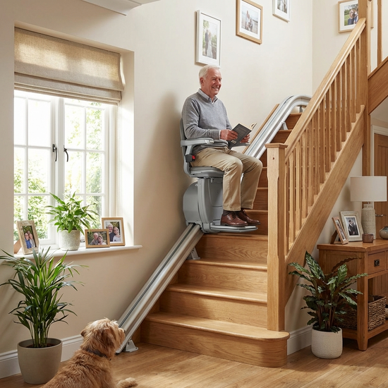 Ein moderner Treppenlift an einer Holztreppe in einem gepflegten Einfamilienhaus. Ein älterer Herr fährt sicher und entspannt nach oben.