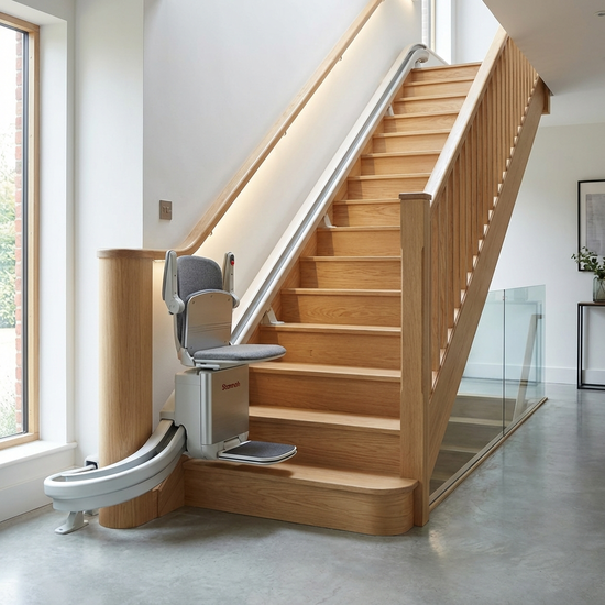 Ein moderner Treppenlift ist an einer hellen, gepflegten Holztreppe in einem stilvollen Einfamilienhaus installiert. Sauber, sicher, gut beleuchtete Umgebung ohne Personen.