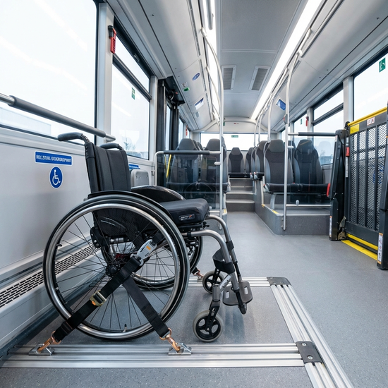 Ein professionell gesicherter Rollstuhl steht im Innenraum eines modernen Transportbusses, befestigt mit einem sicheren 4-Punkt-Gurtsystem auf stabilen Bodenschienen.