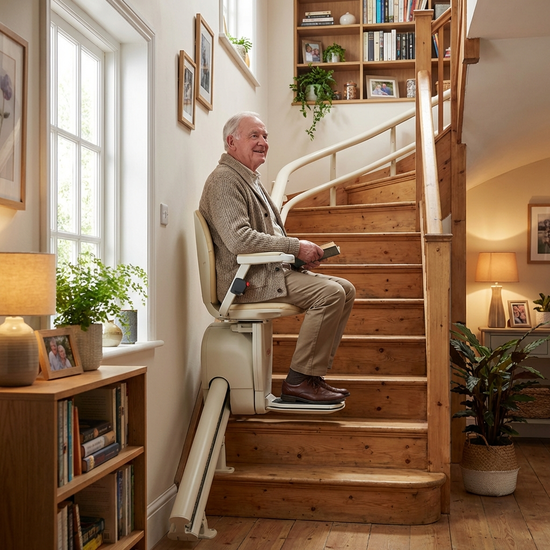 Ein älterer Mann fährt entspannt und sicher mit einem modernen Treppenlift eine gut beleuchtete Holztreppe im eigenen Haus hinauf.