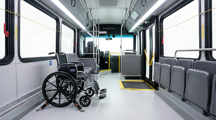 Ein detaillierter Blick auf das Innere eines modernen Transportbusses für Senioren. Ein Rollstuhl ist sicher mit einem professionellen Vier-Punkt-Gurtsystem am sauberen Fahrzeugboden befestigt. Helle, sichere und aufgeräumte Umgebung.