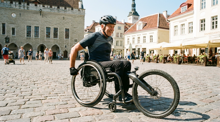 Ein aktiver Senior fährt mit einem wendigen, modernen Adaptivrollstuhl über das historische Kopfsteinpflaster in einer Altstadt. Die Szene ist lebendig, hell und zeigt Selbstbestimmtheit im Alter. Keine Beschriftungen.