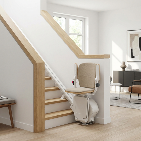 Ein moderner, unauffälliger Treppenlift in einem hellen, gepflegten Einfamilienhaus. Der gepolsterte Sitz ist hochgeklappt und fügt sich harmonisch in das stilvolle Treppenhaus ein.