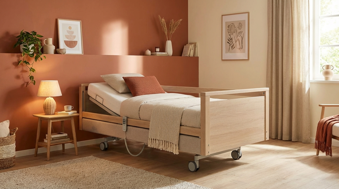 Ein modernes, höhenverstellbares Pflegebett in einem freundlich eingerichteten Schlafzimmer. Neben dem Bett steht ein kleiner Holztisch mit einer Leselampe. Warme Farben, aufgeräumt und einladend, ohne klinische Krankenhaus-Atmosphäre.