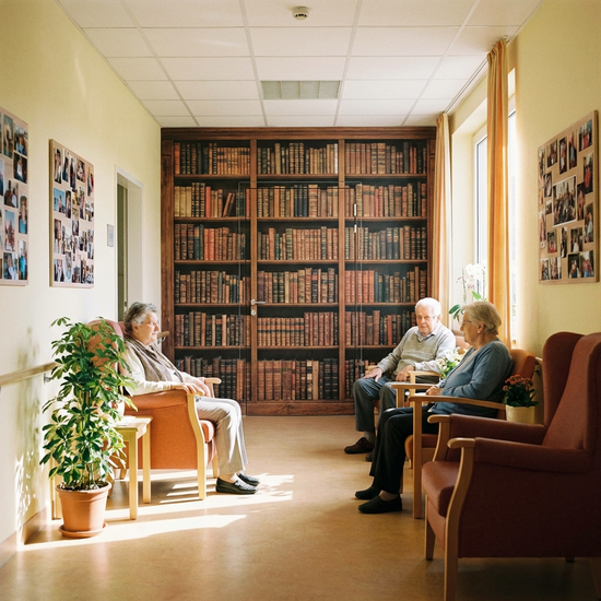 Ein freundlich gestalteter Flur in einer Pflegeeinrichtung, bei dem die Ausgangstür mit einer großflächigen, realistischen Fototapete eines Bücherregals getarnt ist.