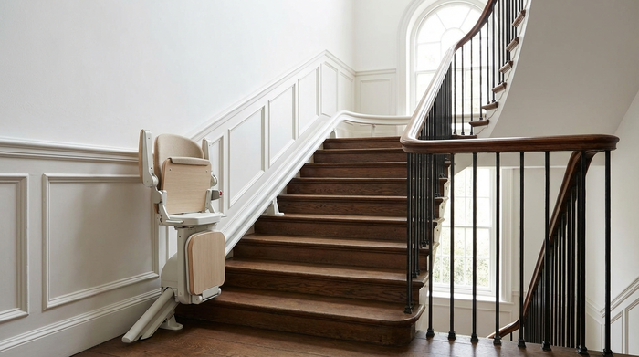 Ein moderner, unauffälliger Treppenlift in einem gepflegten, historischen Treppenhaus mit Holzstufen und weißen Wänden.