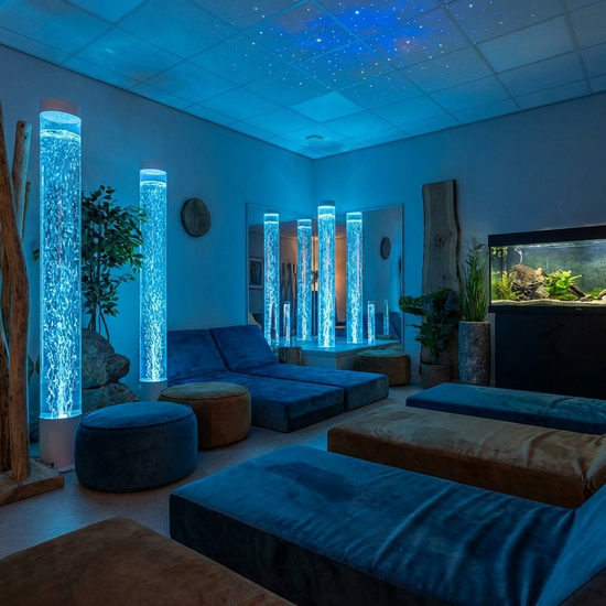 Ein speziell eingerichteter Entspannungsraum mit gedimmtem, beruhigendem blauen Licht, sanft blubbernden Wassersäulen und bequemen Liegematten.