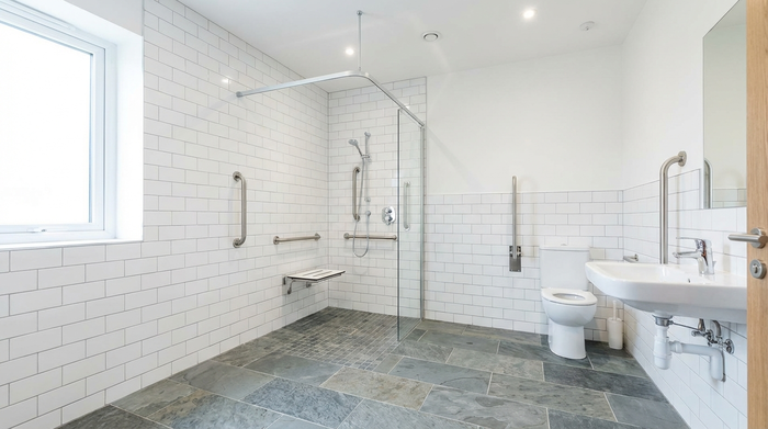 Ein modern umgebautes, barrierefreies Badezimmer mit einer großzügigen, ebenerdigen Dusche, stabilen Haltegriffen an den hellen Wänden und rutschfesten, grauen Fliesen. Hell erleuchtet, sauber, sichere Umgebung für Senioren, absolut textfrei.