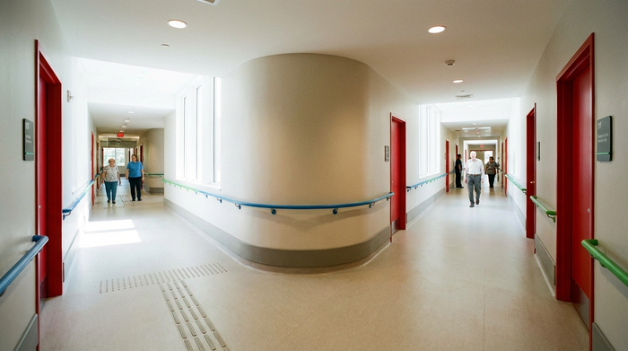 Ein heller, endloser Flur in einer modernen Pflegeeinrichtung mit farblich abgesetzten Handläufen und gut sichtbaren, roten Türen. Demenzgerechte, sichere Architektur ohne Sackgassen.