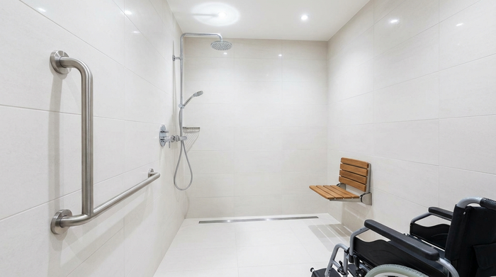 Eine moderne, barrierefreie Dusche in einem hell gefliesten Badezimmer. Ein stabiler Haltegriff ist an der Wand montiert, ein ergonomischer Duschsitz ist sichtbar. Sauber, sicher und gut beleuchtet.