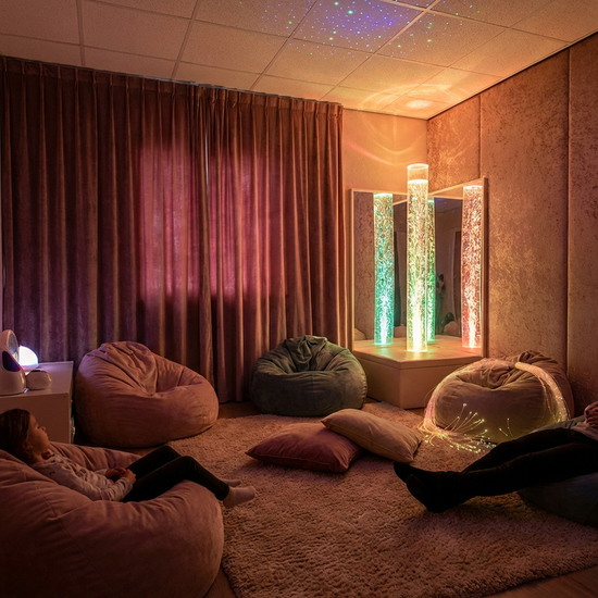 Ein sogenannter Snoezelen-Raum mit gedimmtem Licht, einer leuchtenden Wassersäule und bequemen Sitzsäcken. Die Atmosphäre ist ruhig und entspannend.