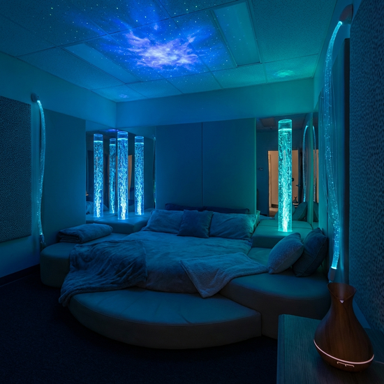 Ein beruhigender Snoezelen-Raum mit gedimmtem Licht, sanften blauen Lichteffekten, einer bequemen Liegelandschaft und leuchtenden Wassersäulen.