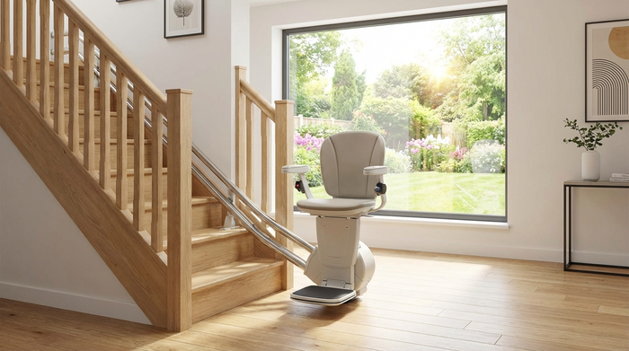 Ein moderner Treppenlift an einer hellen Holztreppe in einem gepflegten Einfamilienhaus. Im Hintergrund ein Fenster mit Blick in den sonnigen Garten.