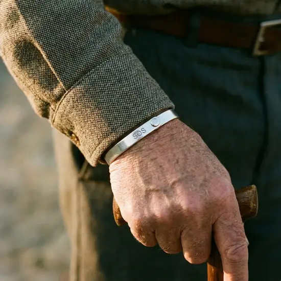 Ein elegantes, silbernes SOS-Armband am Handgelenk eines älteren Mannes, das unauffällig zwischen dem Ärmel seines Hemdes hervorlugt.