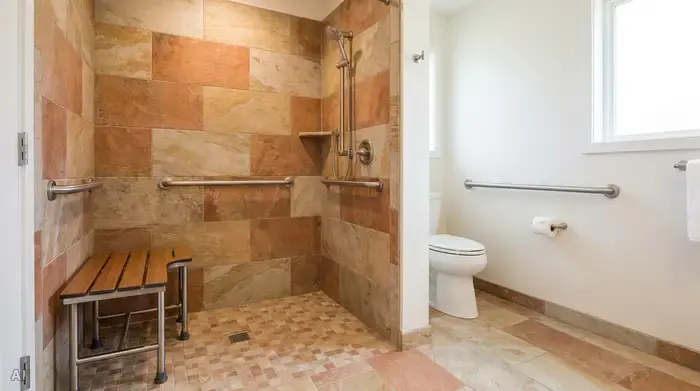 Ein modernes, barrierefreies Badezimmer mit einer großzügigen, bodengleichen Walk-in-Dusche. Ein stabiler Duschhocker steht in der Dusche, rutschfeste Fliesen in warmen Erdtönen bedecken den Boden. Haltegriffe an der Wand sorgen für Sicherheit. Helles, sauberes Ambiente.