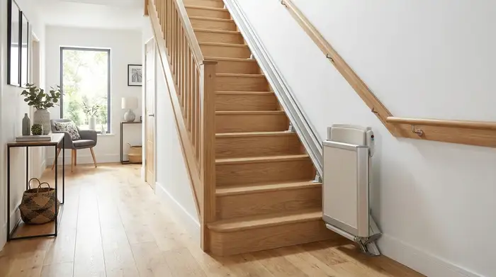 Ein moderner, unauffälliger Treppenlift an einer hellen Holztreppe in einem gepflegten Einfamilienhaus. Ein sicherer Handlauf an der Wand ist gut sichtbar.