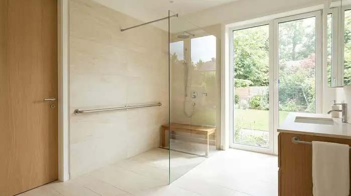 Ein modernes, barrierefreies Badezimmer mit einer großzügigen, bodengleichen Dusche, hellen Fliesen, einem dezenten Haltegriff an der Wand und viel natürlichem Licht.