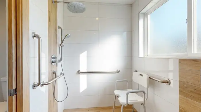 Eine moderne, barrierefreie, ebenerdige Dusche in einem hellen Badezimmer mit stabilen Haltegriffen an der Wand und einem sicheren, weißen Duschhocker.