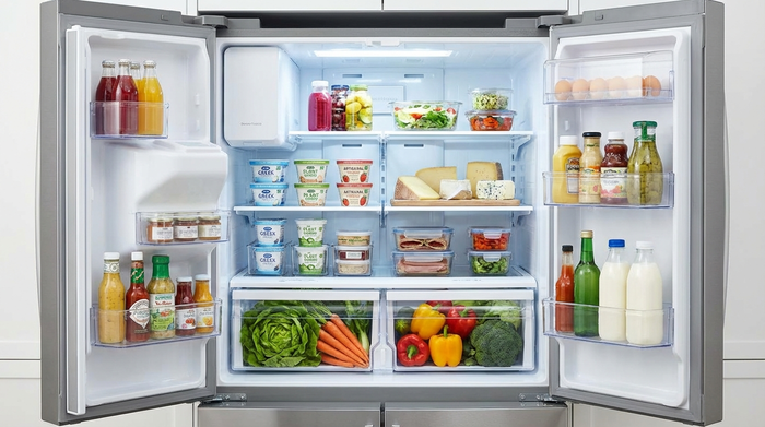 Ein geöffneter, aufgeräumter Kühlschrank mit verschiedenen Fächern. Frisches Gemüse liegt in der unteren Schublade, Joghurt und Käse in der Mitte. Helle, saubere Beleuchtung.