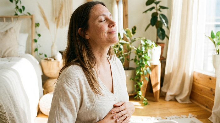 Eine Nahaufnahme einer entspannten Frau, die in einem hellen Raum tief durchatmet, die Hände sanft auf dem Bauch liegend. Friedliche, warme Ausstrahlung, realistischer Stil ohne Text.