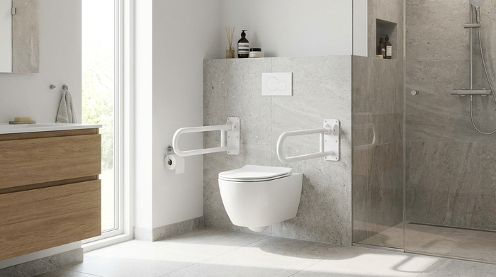 Ein erhöht montiertes, modernes Wand-WC in einem hellen Badezimmer. An beiden Seiten der Toilette sind stabile, weiße Stützklappgriffe fest in der Wand verankert.