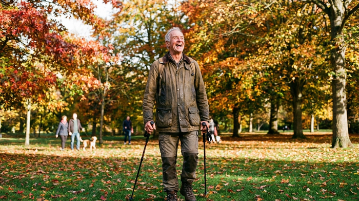 Ein rüstiger Senior spaziert lächelnd durch einen herbstlichen Park, atmet tief die frische Luft ein und wirkt vital und voller Energie.