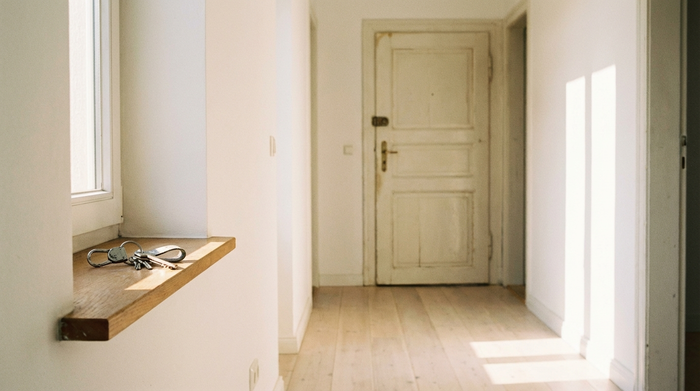 Ein sauberer, leerer Flur in einer hellen Wohnung. Ein silberner Schlüsselbund liegt auf einem kleinen Fensterbrett im warmen Sonnenlicht. Ruhige und aufgeräumte Szene.