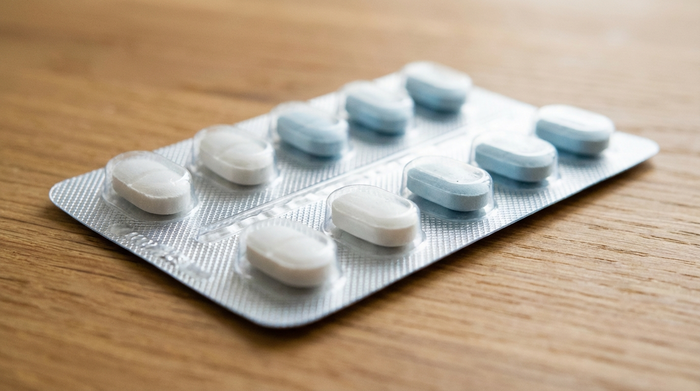 Nahaufnahme von unversehrten, weißen und hellblauen Tabletten in einem glänzenden, silbernen Blister auf einem sauberen Holztisch. Das Licht reflektiert sanft auf der unbeschädigten Folie.