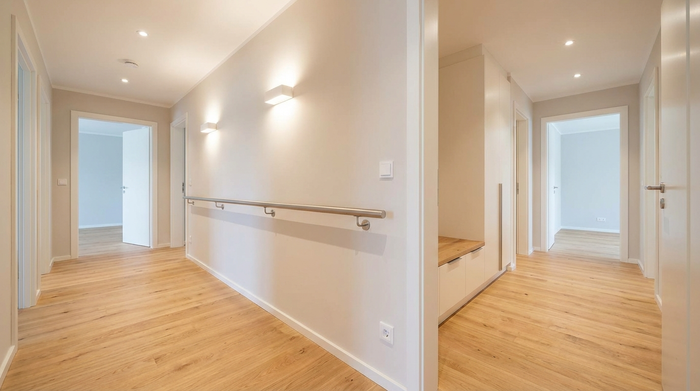 Ein gut ausgeleuchteter, barrierefreier Flur in einem modernen Zuhause. Keine Stolperfallen, ein heller Holzboden und ein dezenter, stabiler Haltegriff an der Wand sorgen für maximale Sicherheit.