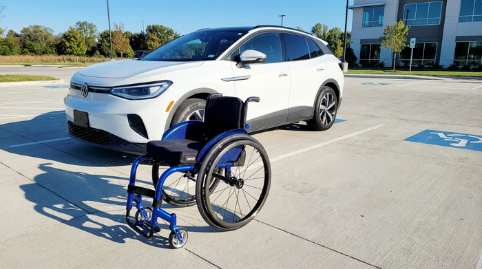 Ein moderner blauer Rollstuhl steht gut sichtbar neben einem geparkten Auto auf einem breiten, sauberen Parkplatz an einem sonnigen Tag.