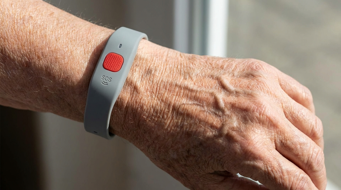 Eine Nahaufnahme des Handgelenks einer älteren Person, die ein unauffälliges, modernes Hausnotruf-Armband mit einem deutlich erkennbaren roten Notfallknopf trägt.