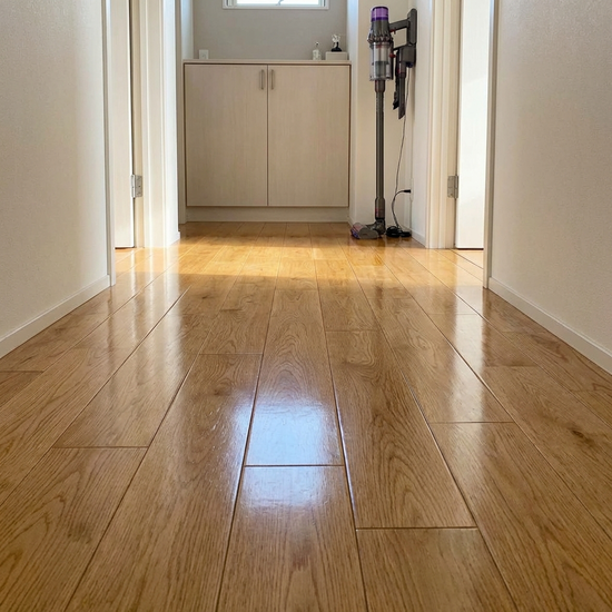 Ein sauberer, glänzender Holzboden in einem aufgeräumten Flur, im Hintergrund steht ein moderner Staubsauger bereit für die Hausarbeit.