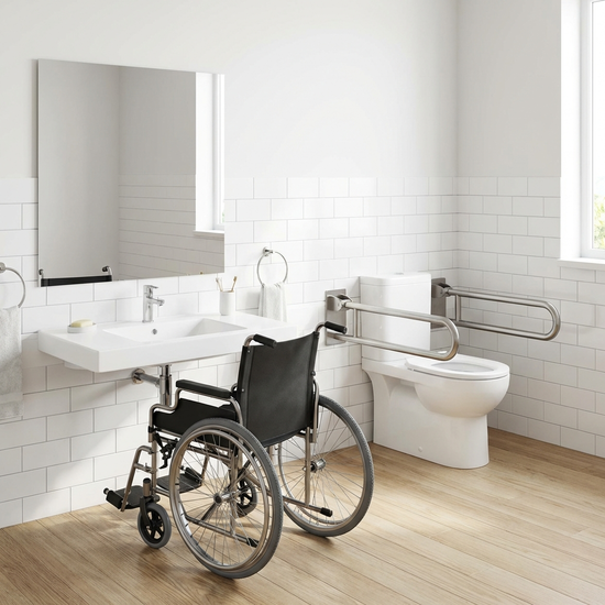 Ein unterfahrbares, weißes Waschbecken in einem sauberen Badezimmer. Ein flacher Spiegel hängt auf Sitzhöhe. Daneben befindet sich eine erhöhte Toilette mit beidseitigen, stabilen Stützklappgriffen.